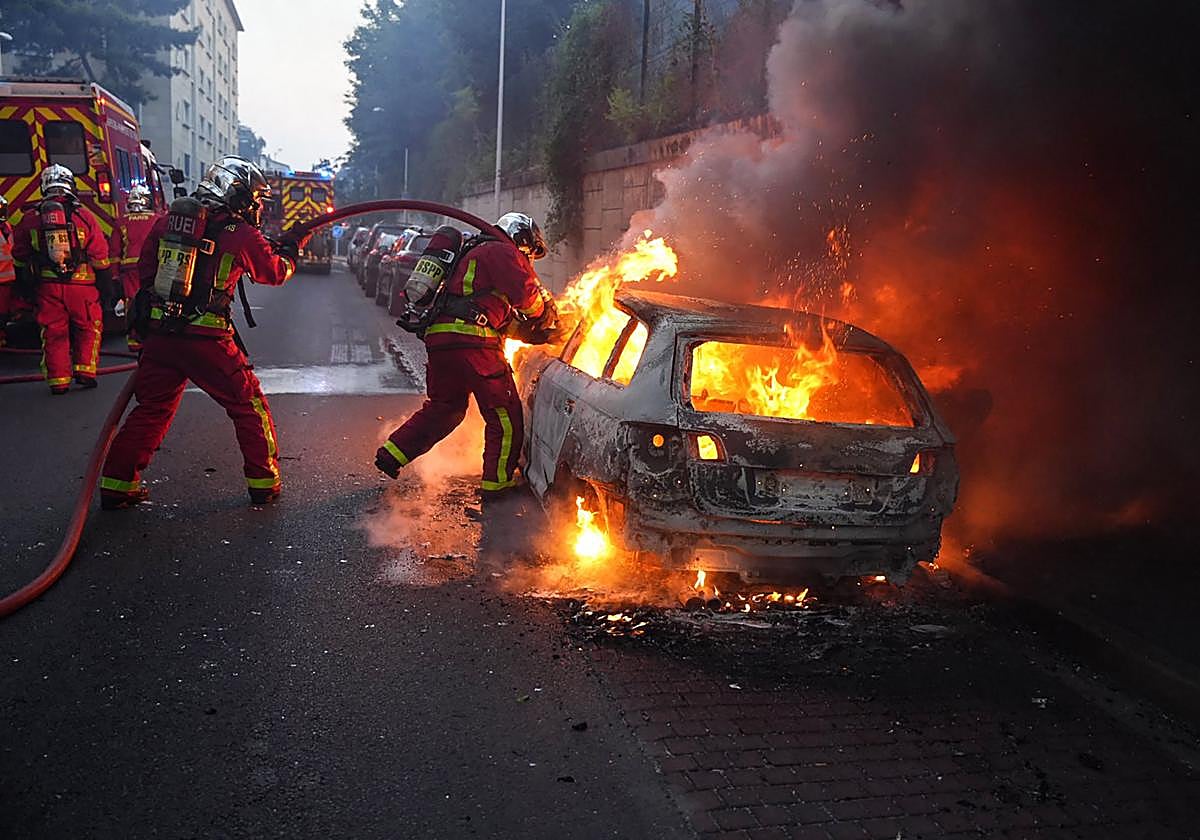 Los bomberos trabajan para apagar un automóvil en llamas al margen de una manifestación en Nanterre