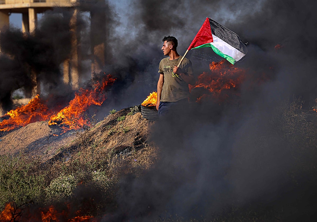 Un joven palestino sostiene una bandera junto a neumáticos ardiendo durante una protesta junto a la valla fronteriza