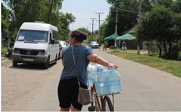 Imagen principal - Serhiy camina entre sus viñedos (IZQ). Reparto de bidones de agua en Nikopol (DRCH.) Vecina lleva varias garrafas de agua (Arriba)