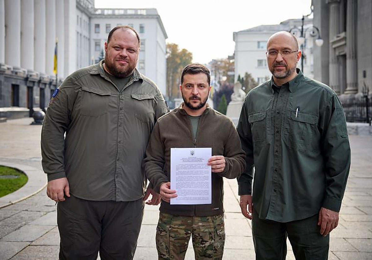 El presidente de Ucrania, Volodímir Zelenski (centro), el primer ministro de Ucrania, Denis Shmihal (derecha), y el presidente del parlamento de Ucrania, Ruslan Stefanchuk (izquierda), posan con el documento que solicita la membresía acelerada de la OTANAFP