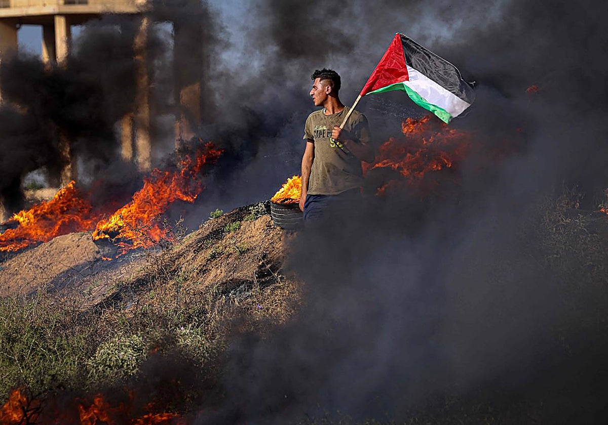 Un joven palestino sostiene una bandera junto a neumáticos ardiendo durante una protesta junto a la valla fronteriza con Israel