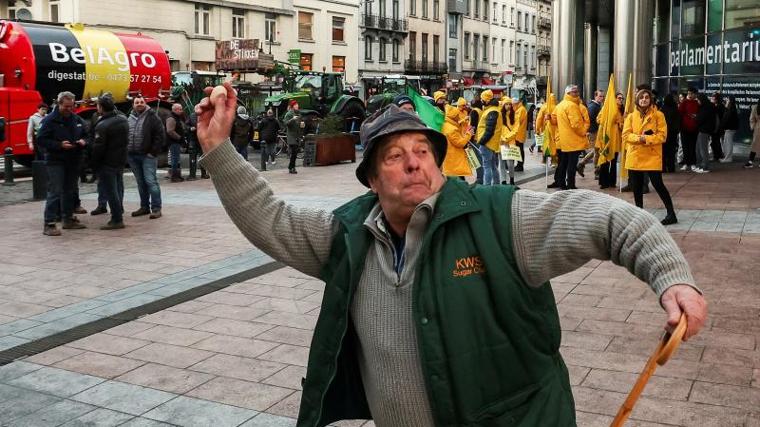 Un agricultor lanza un huevo a los agentes de policía durante unas protestas que buscan bloquear el exterior de la sede de la Unión Europea