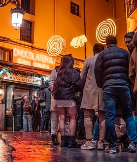 Imagen secundaria 2 - Arriba, el callejón de San Ginés con un siglo de diferencia. Sobre estas líneas, Pedro Trapote, actual dueño del negocio y una larga cola de jóvenes que esperan su chocolate con churros el día de nochevieja. 