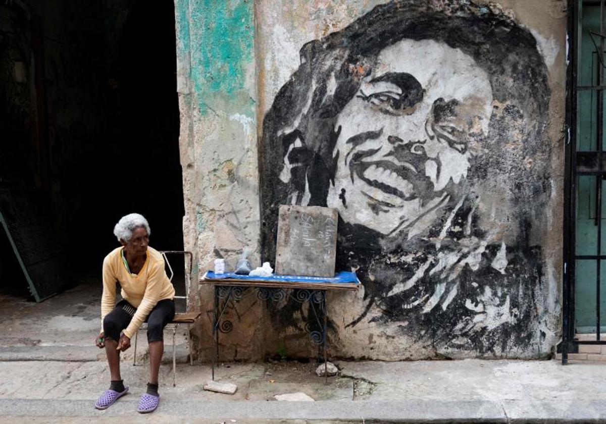 Una anciana vende frijoles y cigarrillos junto a un mural que representa al cantante jamaicano Bob Marley en una calle de La Habana