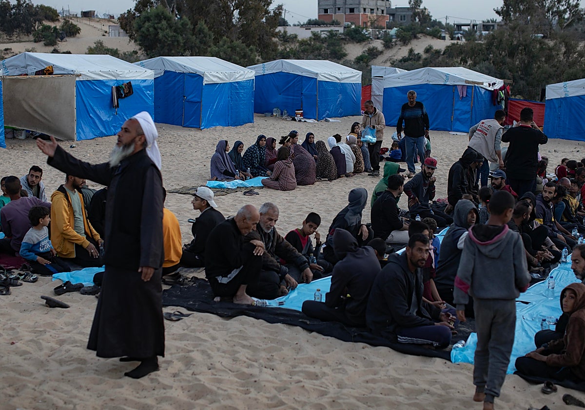 Desplazados sentados juntos junto a sus tiendas para comer durante el mes sagrado del Ramadán en una comida colectiva de Iftar organizada por un grupo de jóvenes voluntarios en el campamento de Rafah