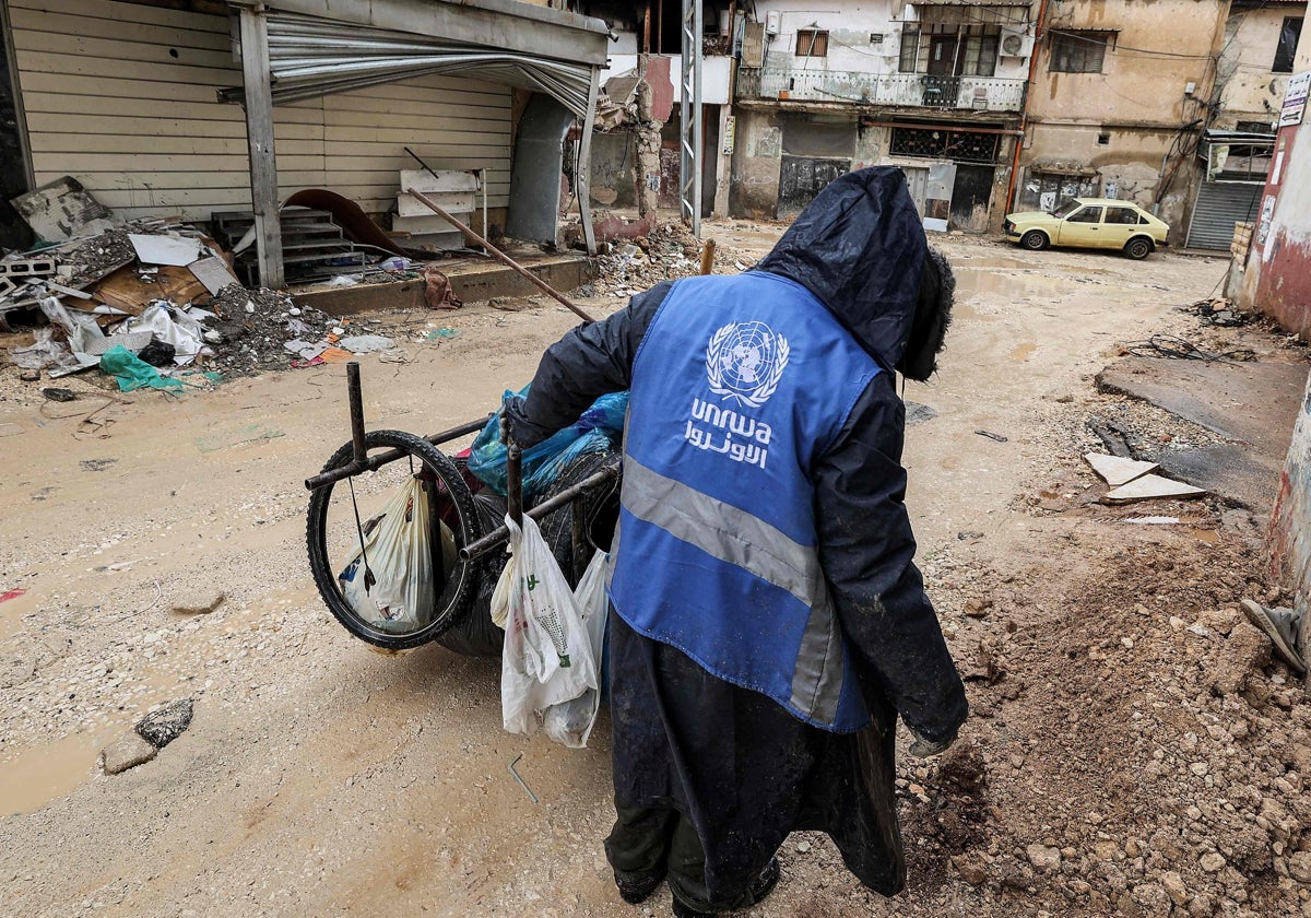 Un hombre vestido con una chaqueta de la Unrwa recoge basura en una calle de Cisjordania