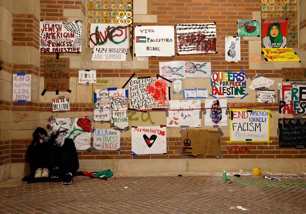 Un par de manifestantes duermen bajo un muro cubierto de pancartas cerca de un campamento instalado por estudiantes y activistas pro-palestinos en el campus de la Universidad de California