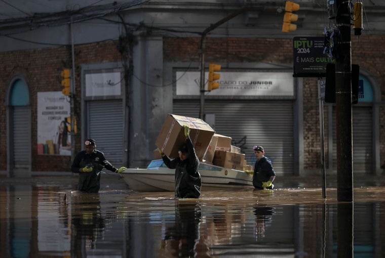 Hombres cargan y mueven paquetes a lo largo de una calle inundada en el centro histórico de la ciudad de Porto Alegre