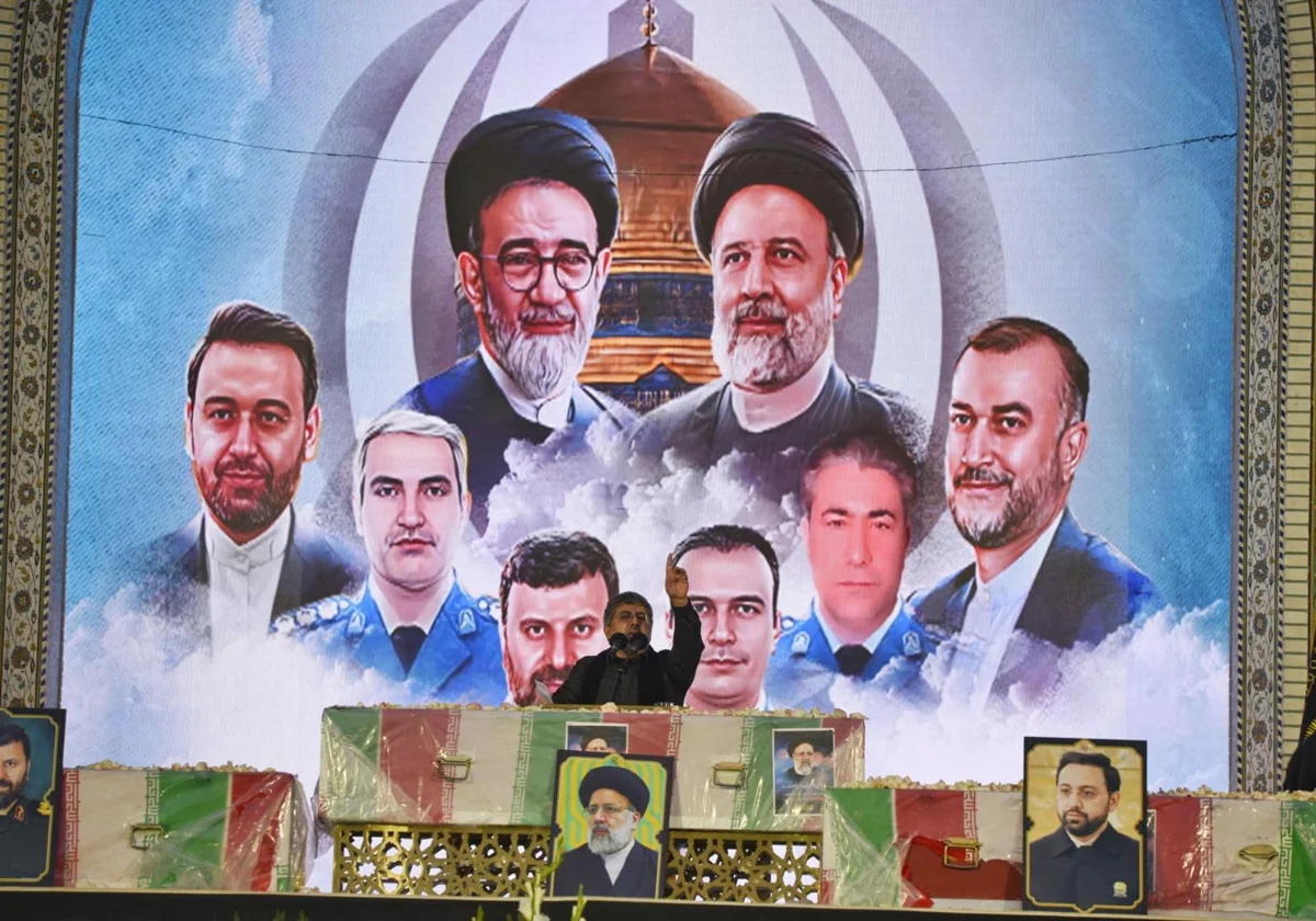 Un iraní lee una oración sobre el ataúd del difunto presidente Ebrahim Raisi, con el fondo de un mural de quienes murieron con él en un accidente de helicóptero