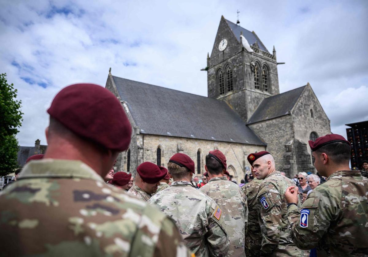 El personal militar estadounidense de una unidad aerotransportada se reúne al pie de la iglesia en la que se encuentra una efigie del veterano de la Segunda Guerra Mundial, el 82º paracaidista aerotransportado del ejército estadounidense, John Steele