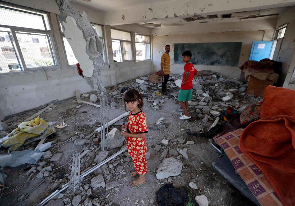 Una niña palestina junto a su hermano en el aula destruida de una escuela del campamento de Shati