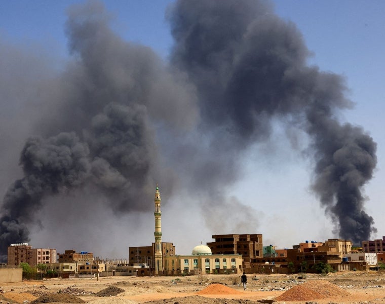 Un hombre camina mientras el humo se eleva sobre los edificios después de un bombardeo aéreo, durante enfrentamientos entre las Fuerzas paramilitares de Apoyo Rápido y el Ejército en Jartum Norte