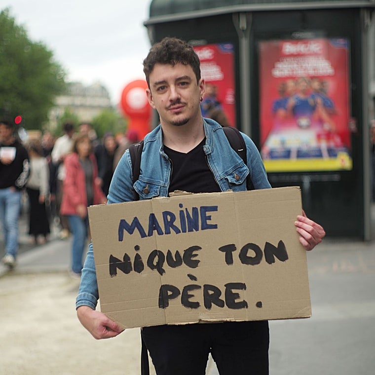 Un joven sostiene un cartel que dice «Marine, fóllate a tu padre»