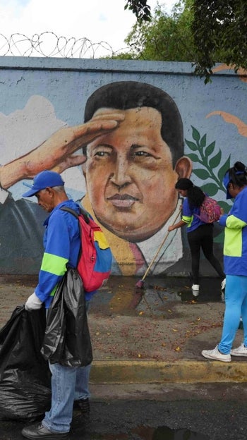 Trabajadores limpian frente a un mural con la imagen de Chávez