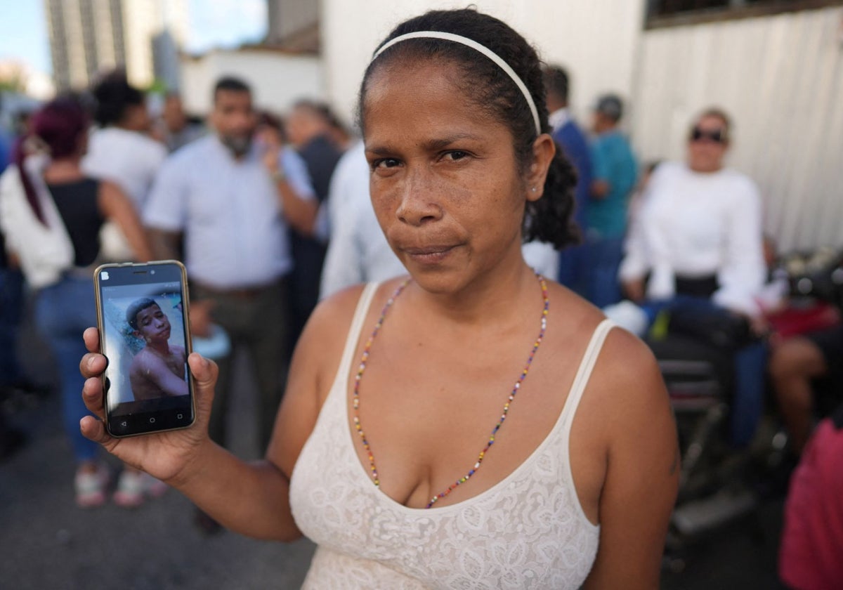 Una mujer sostiene un teléfono móvil con la fotografía de su hijo, detenido por el régimen de Venezuela