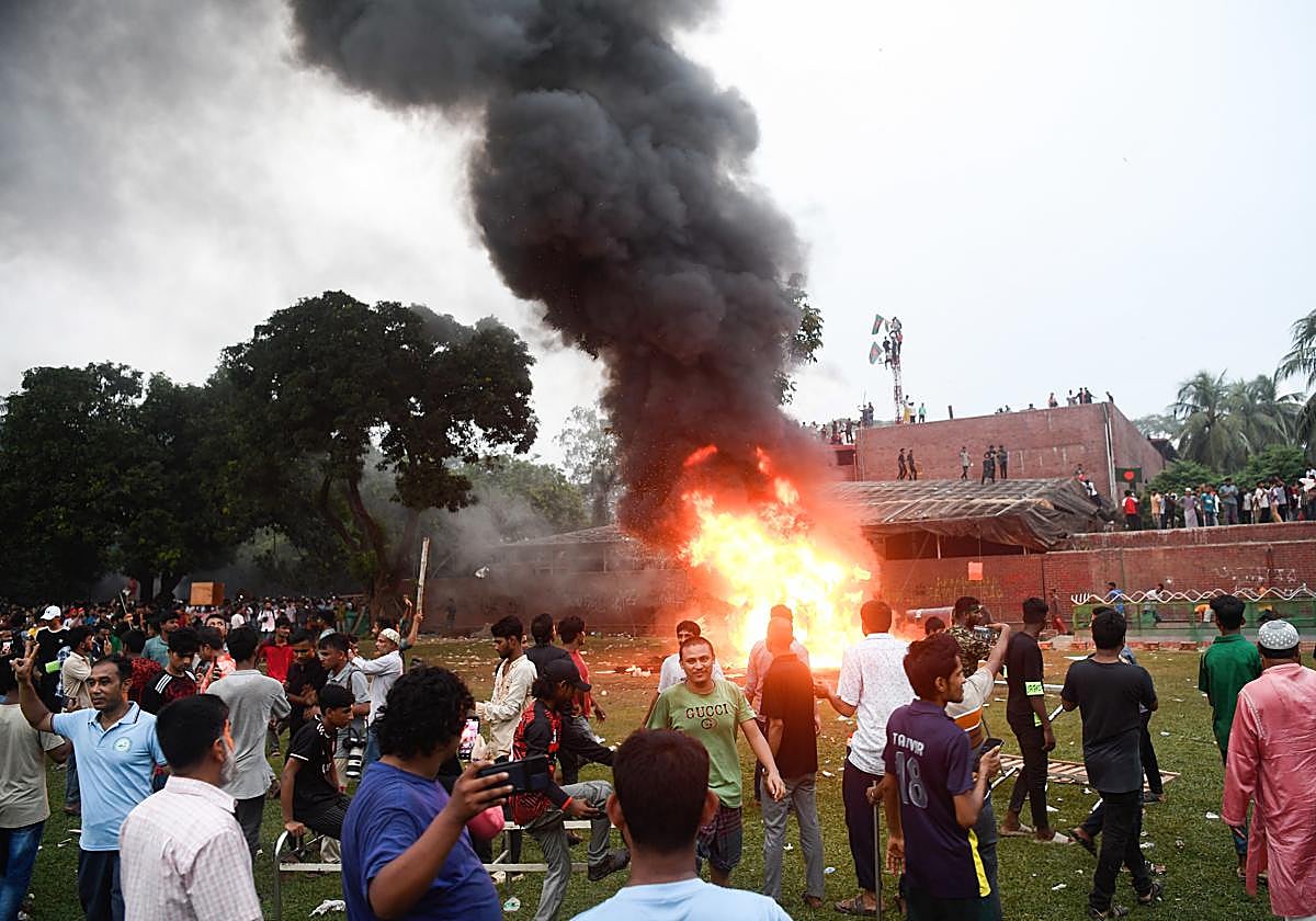 Un coche arde en Ganobhaban mientras la gente se reúne en la residencia de la ex primera ministra Hasina.