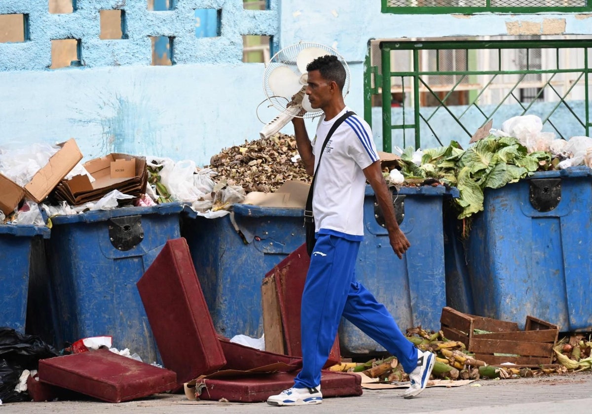 Un hombre camina con un ventilador junto a contenedores de basura durante el tercer día de un apagón masivo