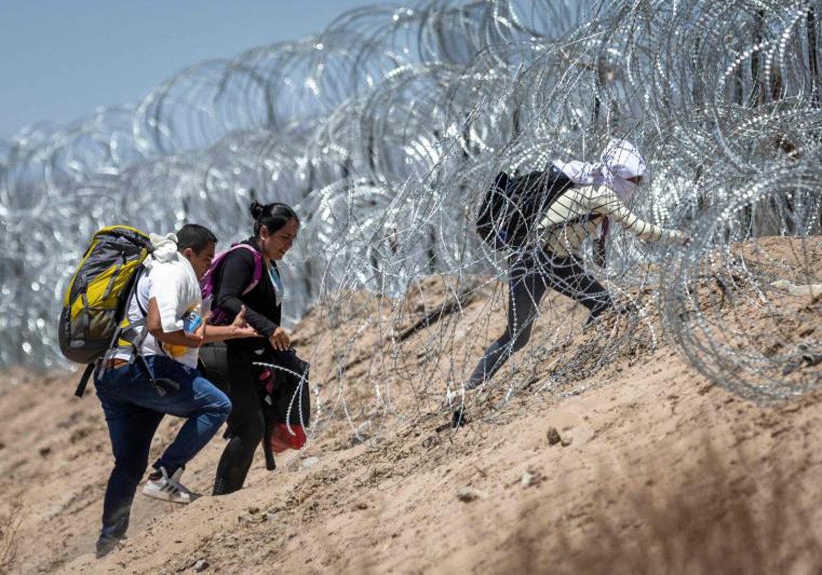 Inmigrantes caminan a través de alambre de púas cerca de El Paso