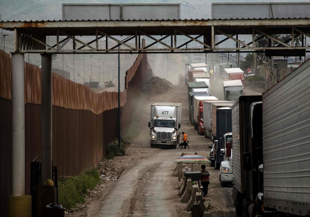 Camiones de mercancías hacen cola junto al muro que separa la frontera entre EE.UU. y México