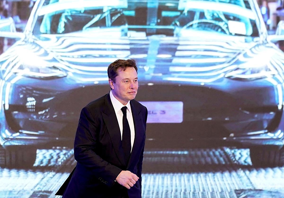 Elon Musk pasa delante de una imagen de un Tesla Model 3