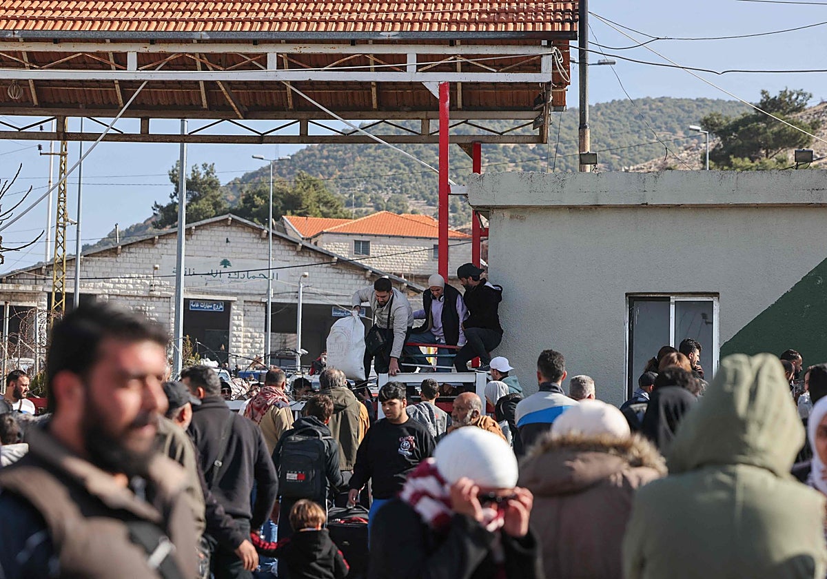 Los viajeros procedentes de Siria saltan una valla de seguridad mientras esperan ser procesados en el cruce fronterizo libanés de Masnaa