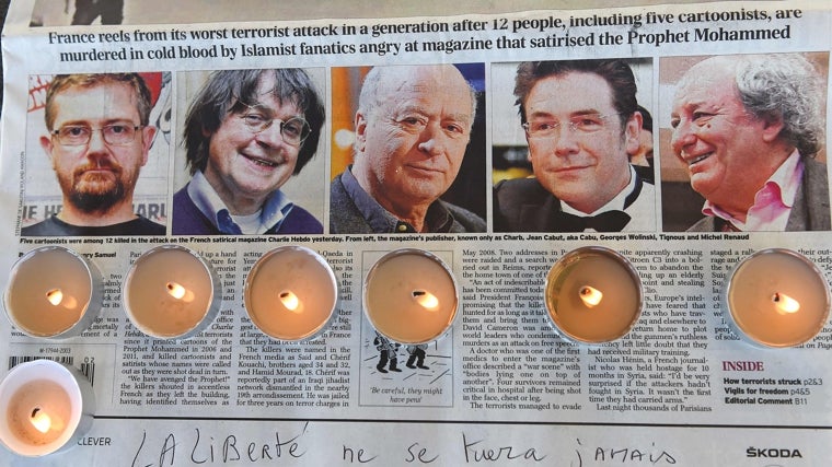 Se colocan velas en un periódico con fotografías del editor del semanario satírico francés 'Charlie Hebdo' y el resto de miembros de la redacción asesinados el 7 de enero de 2015