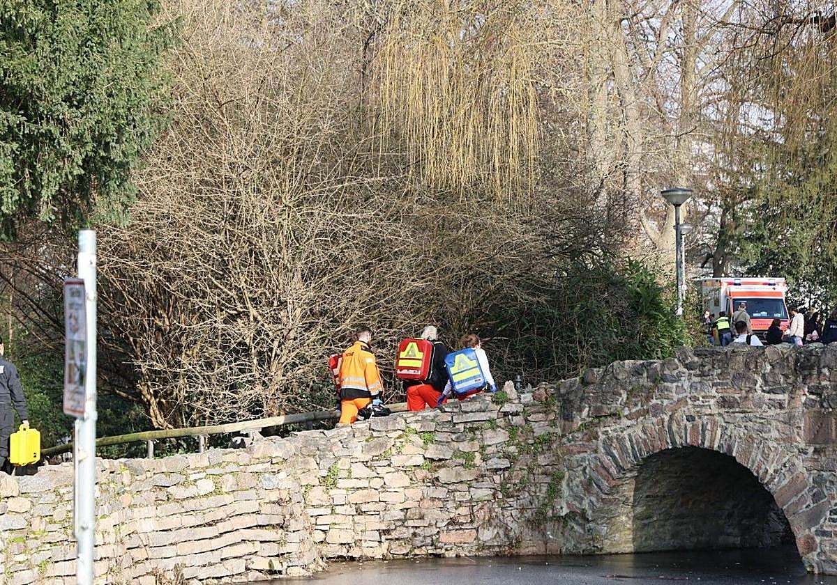 Trabajadores de rescate y técnicos forenses caminan por un pequeño puente cerca del lugar de un apuñalamiento en Aschaffenburg.