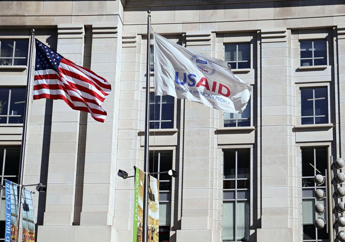 Dos banderas ondean en la entrada de un edificio, a la izquierda la badera de Estados Unidos y a la derecha otra de la USAID