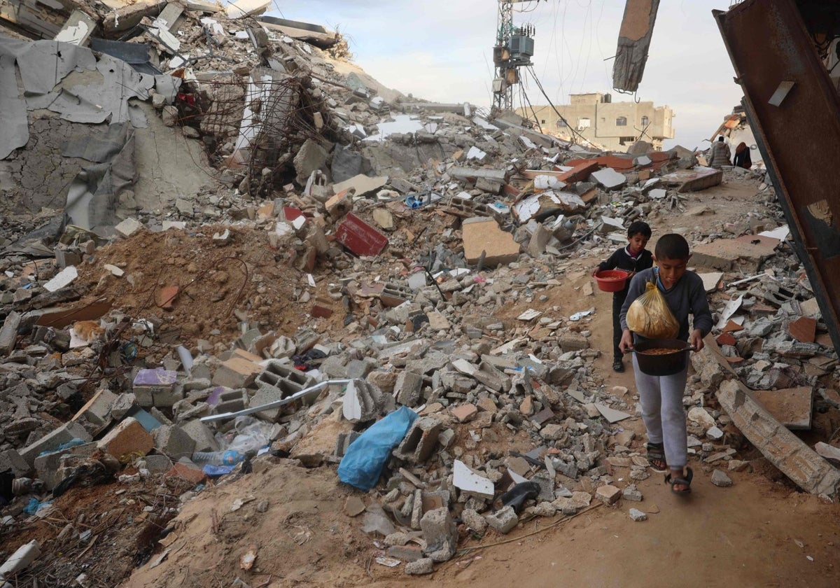 Niños palestinos llevan comida junto a edificios destruidos en el campo de refugiados de Nuseirat, en el centro de la Franja de Gaza