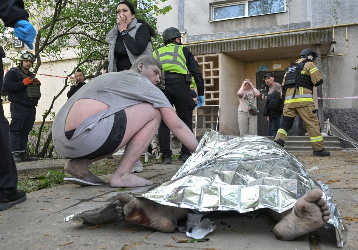 Un residente herido se sienta junto al cuerpo de su madre en el lugar donde un edificio de apartamentos fue alcanzado por un ataque aéreo ruso, en medio del ataque ruso contra Ucrania, en Zaporiyia