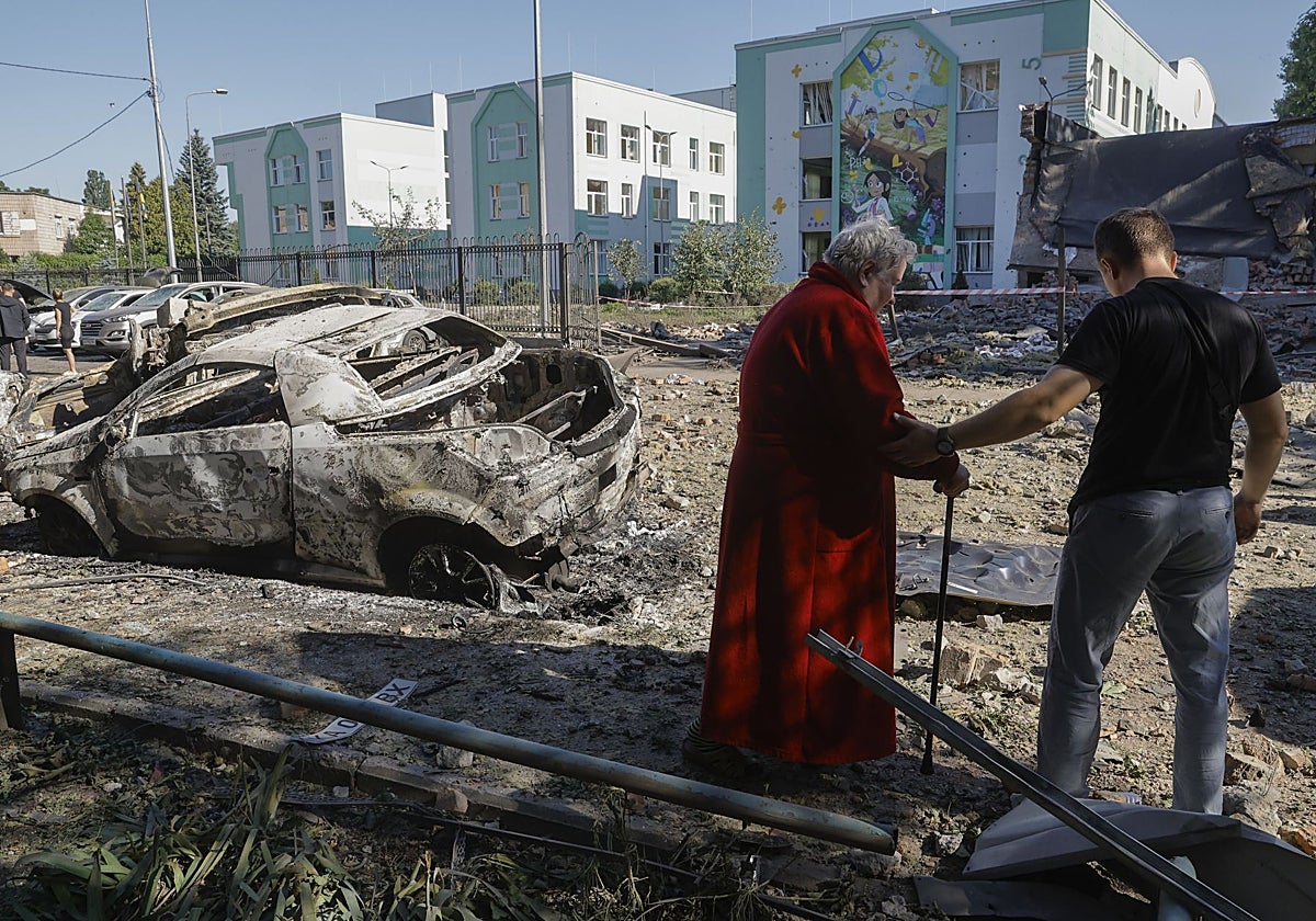 Residentes caminan por una zona dañada con coches destrozados cerca de un edificio escolar tras un ataque aéreo ruso en Kiev