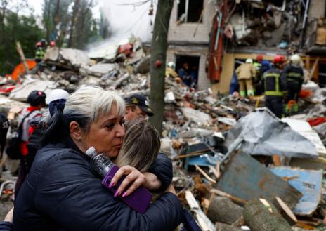 Imagen secundaria 1 - En la primera imagen, un coche en llamas tras el ataque ruso sobre Kiev. Una mujer abraza a otra mientras espera a que su hijo sea rescatado de entre los escombros, en la segunda foto. En la tercera imagen: la primera ministra ucraniana, Yulia Svyrydenko, y el ministro del Interior, Ihor Klymenko, caminan por los escombros que ha dejado el ataque ruso
