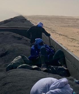 Imagen secundaria 2 - Un mar de pateras inunda el puerto de Nuadibú (imagen superior horizontal). La multitud se aloja para comprar pescado en la lonja de Nuakchot (imagen inferior horizontal). Jóvenes polizones cruzan el Sahara en el 'tren del hierro' para llegar a las costas de Mauritania (imagen vertical)