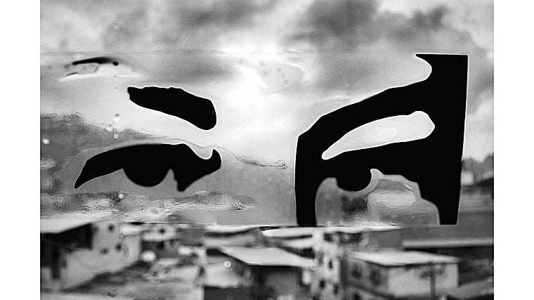 Unos ojos pintados, reproducidos en vinilo, se superponen a la vista de un barrio popular. La mirada, severa y omnipresente, parece flotar sobre los techos de zinc