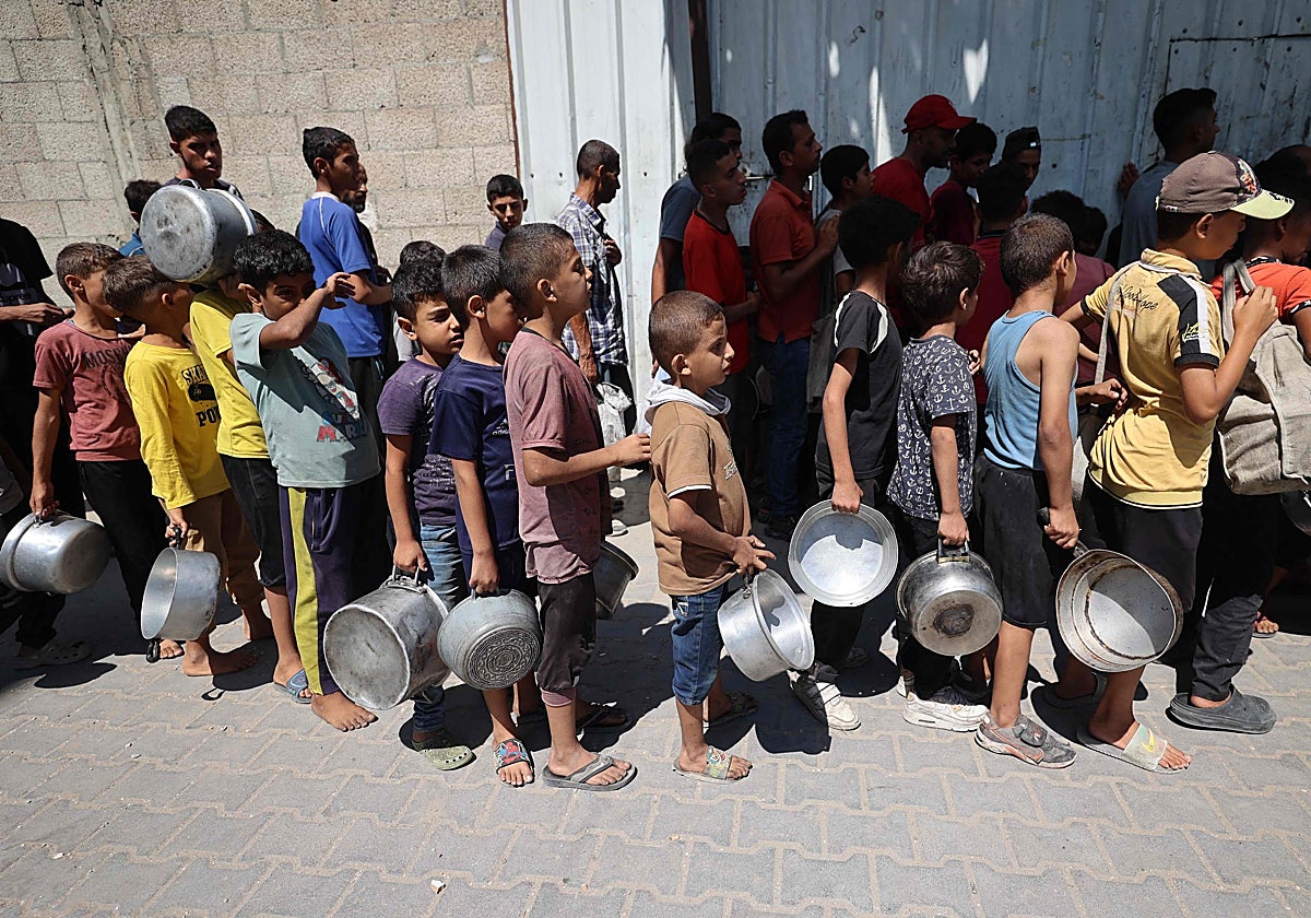 Niños palestinos guardan fila para recibir comida, en la franja de Gaza