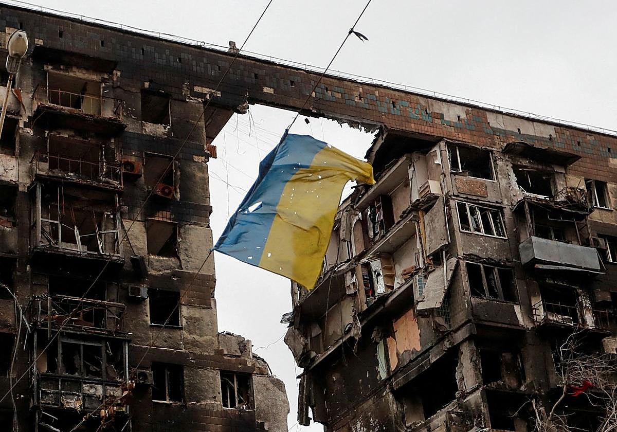 una bandera rota de Ucrania colgada de un alambre frente a un edificio de apartamentos destruido durante el conflicto entre Ucrania y Rusia
