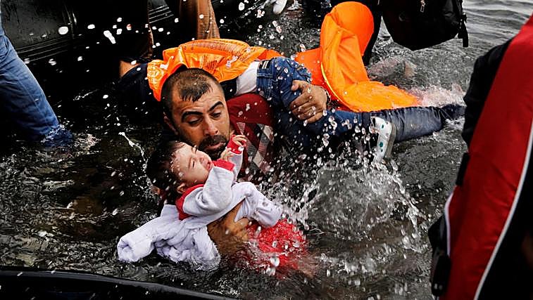 Un refugiado sirio trata de sostener a sus dos hijos al desembarcar en Lesbos en 2015