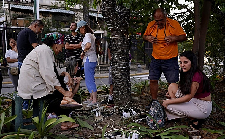Imagen principal - Arriba, la gente carga sus teléfonos tras un apagón en su barrio después de que Estados Unidos atacara Venezuela y capturara a Maduro; debajo a la izquierda, un hombre rescata pertenencias de entre los escombros después del ataque; a la derecha, se puede apreciar cierta normalidad en las calles de Caracas