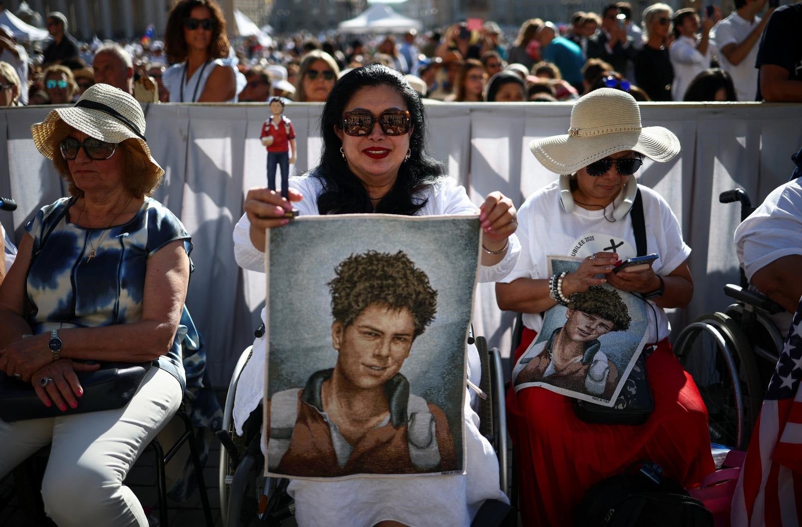 Una mujer sostiene una figura y un tapiz que representa a Carlo Acutis