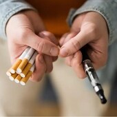 Una persona sujete un cigarrillo electrónico y unos cigarrillos