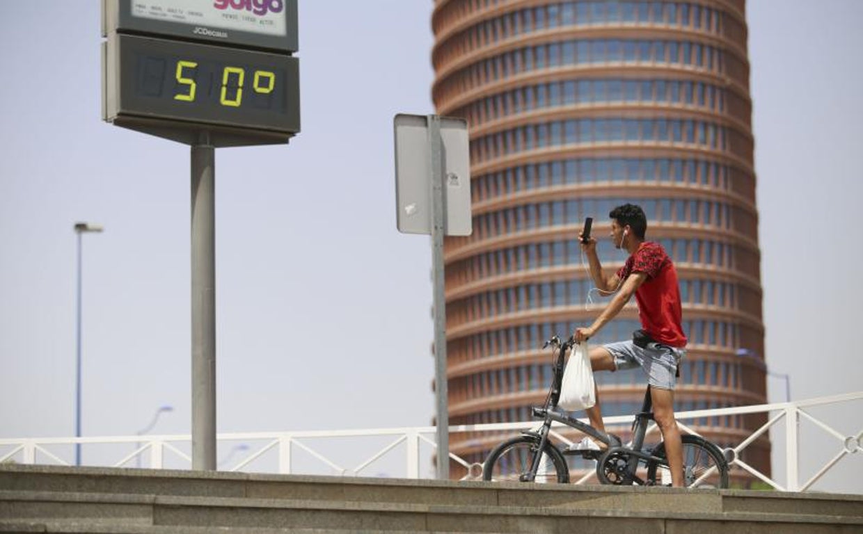 Una persona en bicicleta toma una fotografía de un termómetro junto a la Torre Sevilla