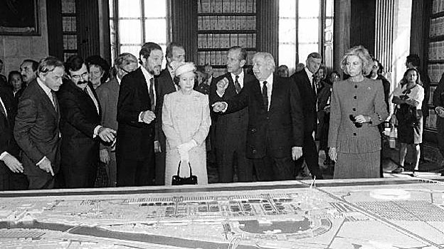 Los Reyes de España y la Reina de Inglaterra junto al duque de Edimburgo atienen den las explicaciones de Manuel Olivencia y Emilio Cassinello sobre la futura Exposición Universal de Sevilla