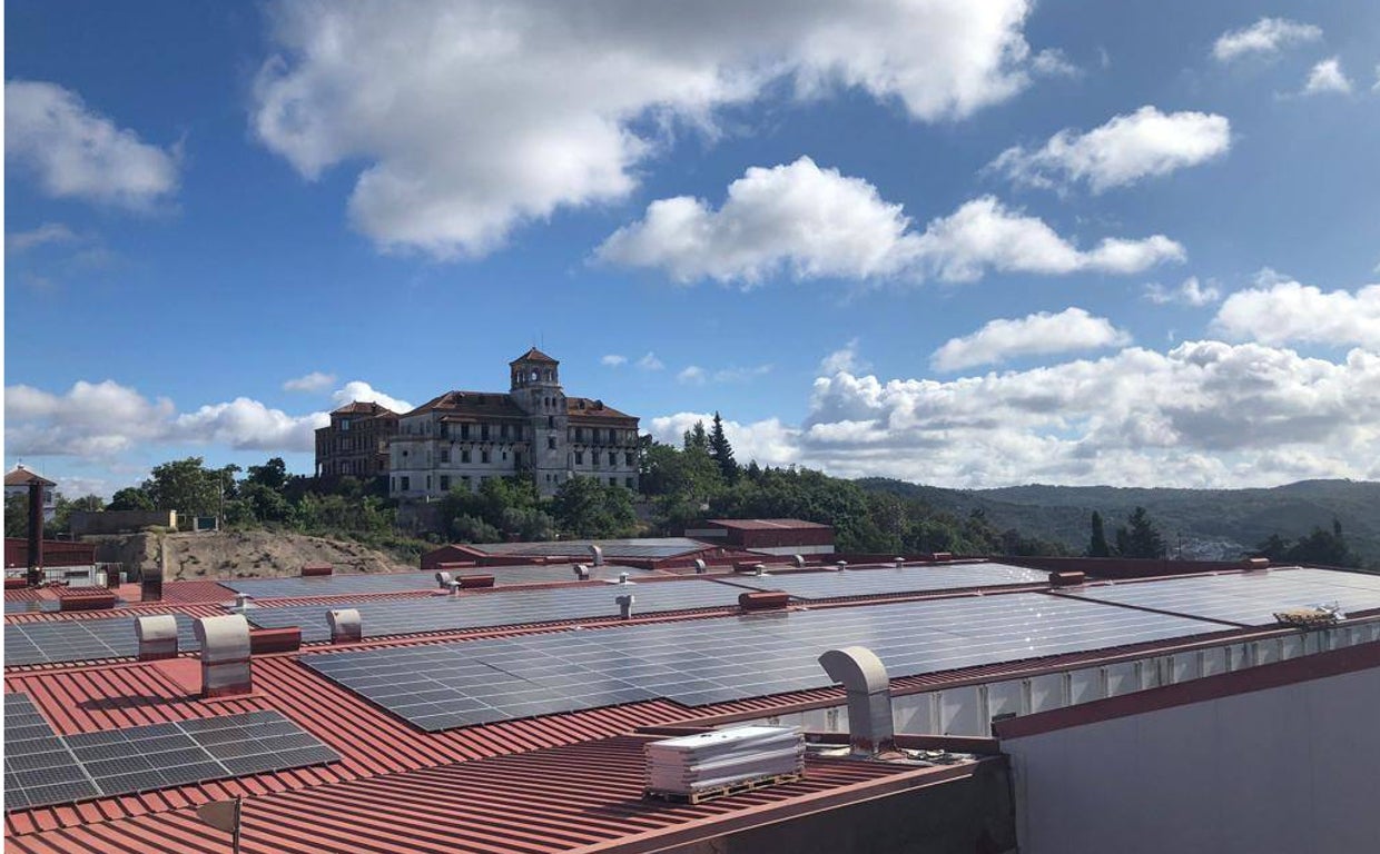 Placas solares en el tejado de la Bodega Cinco Jotas de Jabugo, con el histórico edificio del Tirón Pichón al fondo