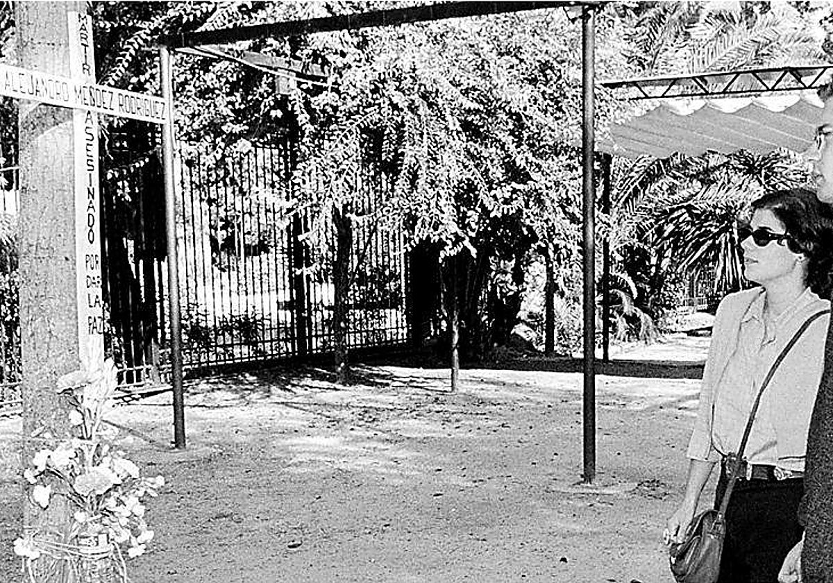 Una pareja contempla la cruz en recuerdo a Alejandro Domingo Méndez, asesinado en los Jardines de Murillo hace 25 años