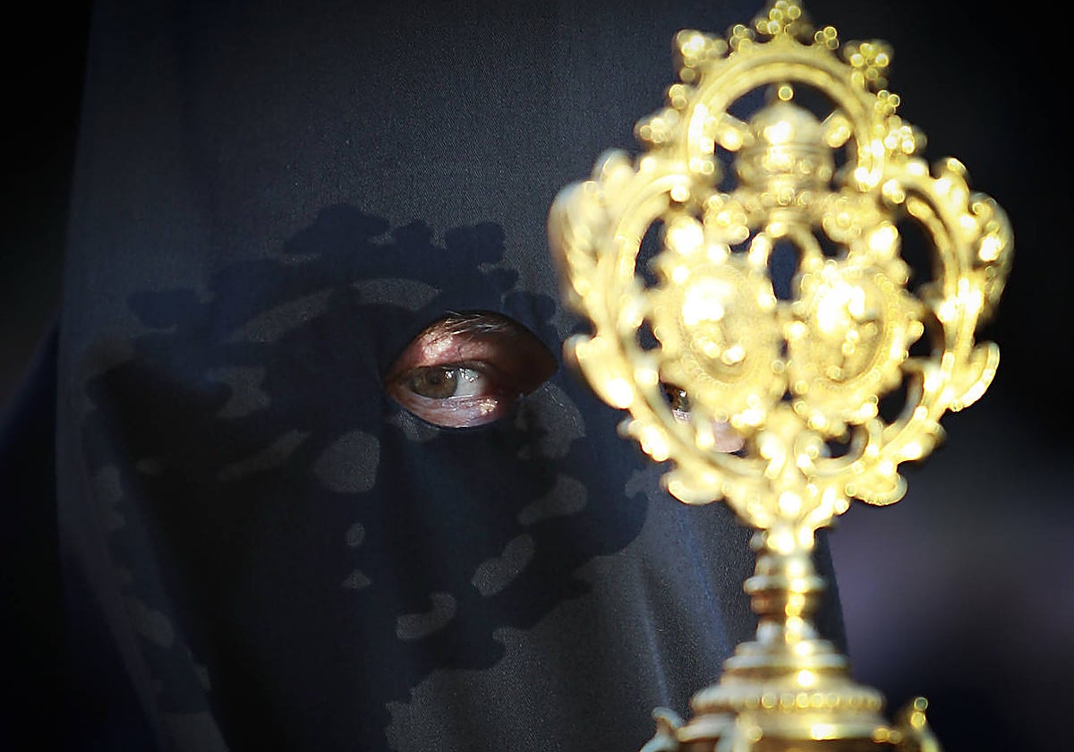 Un nazareno del Cristo de Burgos se hace sombra con la vara dorada