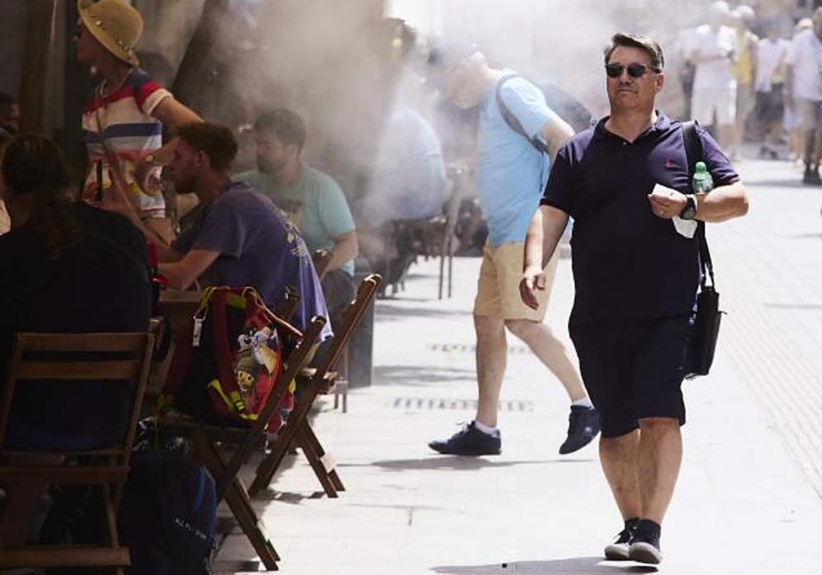 Un señor pasa por debajo de unos aspersores instalados en un bar en el Centro de Sevilla