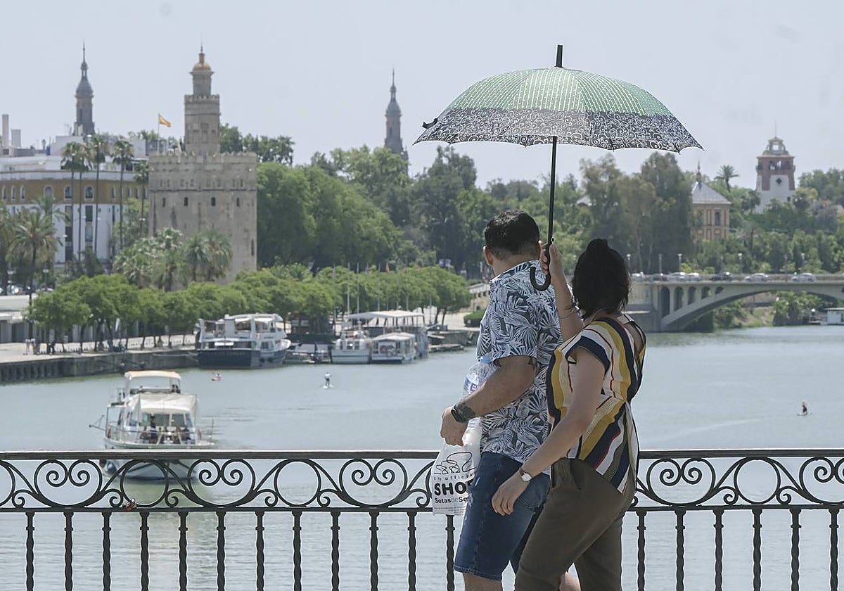 Dos personas se protegen del sol con un paraguas mientras cruzan el puerte de Triana