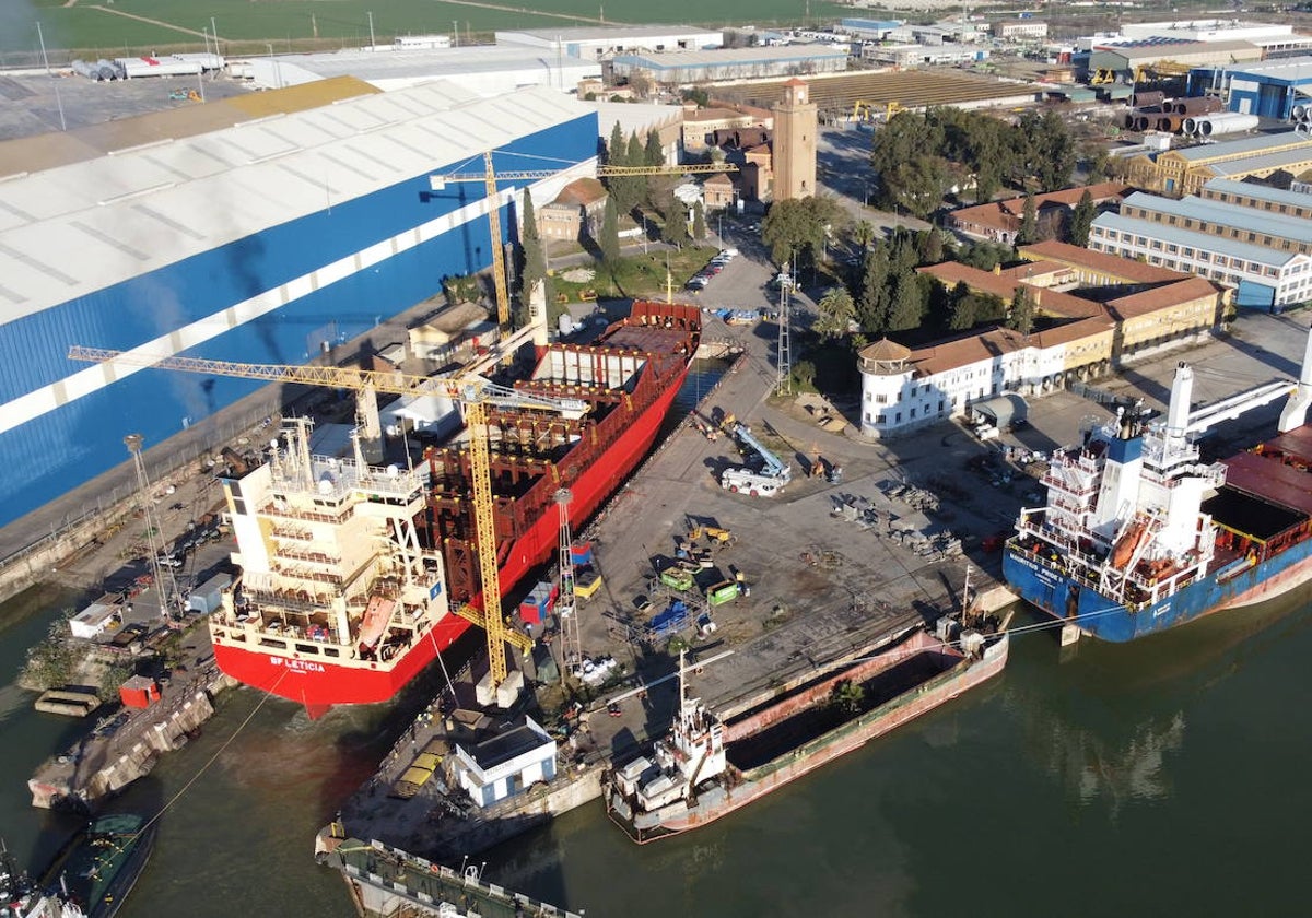 El carguero de color rojo entra en el dique de Astilleros del Guadalquivir para ser reparado, mientras que el azul, en el muelle, espera su turno