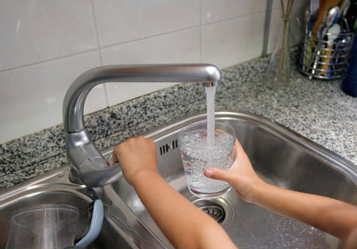 Una persona llena un vaso de agua desde un grifo del fregadero de una cocina