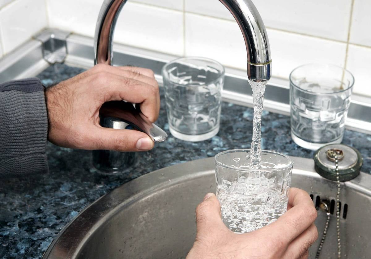 Una persona llena un vaso de agua desde el grifo de una cocina